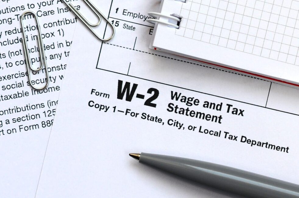 W-2 form surrounded by a notebook, pen, and paperclips