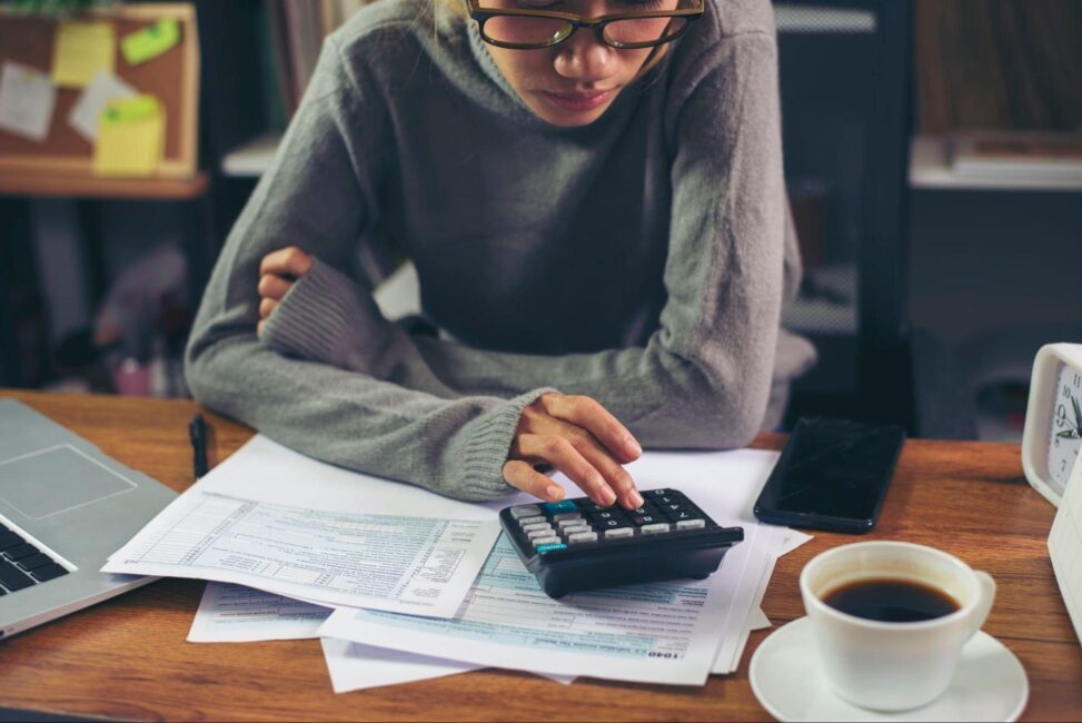 Woman using a calculator to fill out Schedule 1 and tax Form 1040